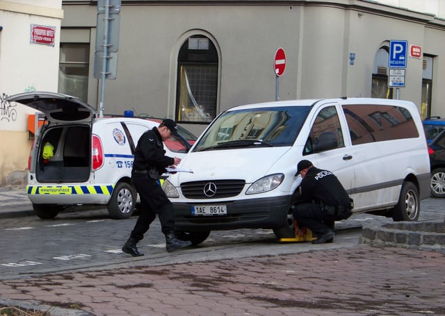 Dva strážníci městské policie nasazují parkovací botičku na dodávku v ulici.