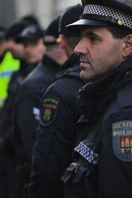 Portrét strážníka v uniformě městské policie; v pozadí jsou další uniformovaní policisté.