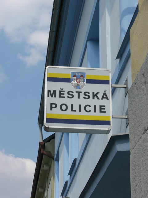 Nástěnná tabule s nápisem „MĚSTSKÁ POLICIE“ a městským znakem.