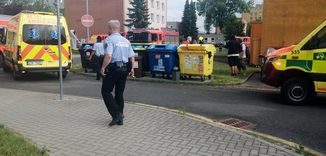 Strážník městské policie stojí poblíž sanitky, hasičského vozidla a dalších zasahujících osob.
